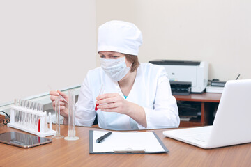 A female doctor in a mask works with blood tests in a biological laboratory