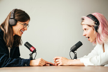 Two woman hosts in local broadcat studio recording audio podcast. Sitting opposite each other