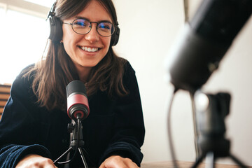 Handsome woman host streaming her audio podcast using microphone at small broadcast studio
