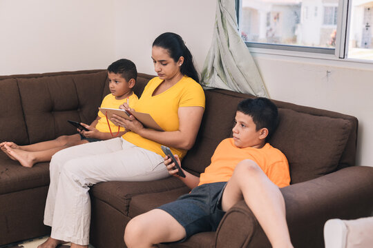 Family Sitting In The Armchair, Mom Checking The Notebook, Son Looking At The Cell Phone