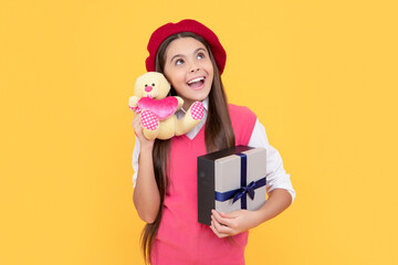 happy teen girl in french beret hold toy present and gift box on yellow background, wow