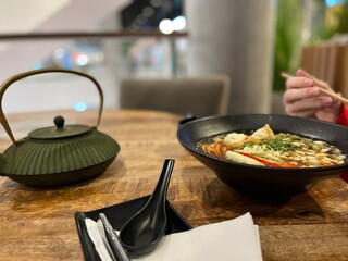 The pleasure of Eating Asian - Kettle with rice tea and hands with chopsticks at the plate with ramen soup