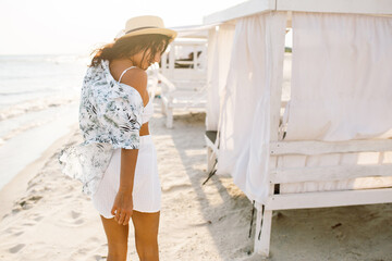 A beautiful woman walks along the beach at sunset. Summer landscape. White sand and blue sea. Deserted beach. Bungalow.