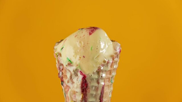 Timelapse of banana ice cream with strawberry topping and colorful sprinkles in waffle cone melting on yellow background. Delicious yellow ice cream melting. Close-up of sweet dessert. Food concept