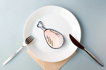 A painted chicken leg lies on a white plate served with a table knife and fork on a gray background. The topic of economic sanctions and food shortages. View from the top point. - obrazy, fototapety, plakaty