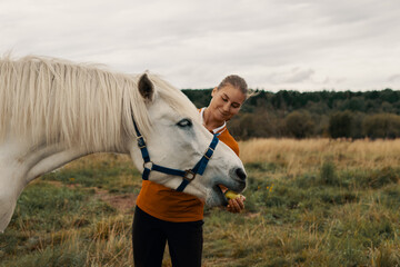 Happy young woman feeding horse with apple from hand in outdoors.