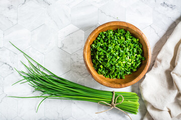 Fresh chopped green onions in a wooden bowl and a bunch of onions on the table. Top view. - obrazy, fototapety, plakaty