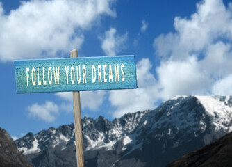 Follow Your Dreams motivational quote on sign in nature.