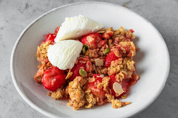 Tasty breakfast. Strawberry crumble with ice cream, almonds and pumpkin seeds in a plate on gray background. close up