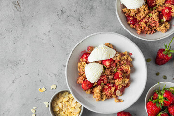 Delicious strawberry crumble with ice cream, almonds and pumpkin seeds in a plate on gray background. Top view