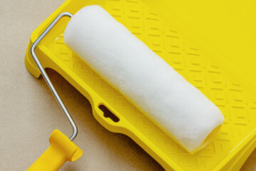 Painting apartment, renovating with white color paint. Paint roller in paint tray with white color in the tray on brown paper