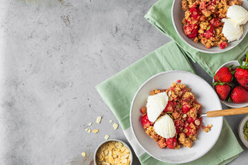 Delicious strawberry crumble with ice cream, almonds and pumpkin seeds in a plate with spoon on gray background
