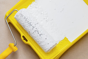 Painting apartment, renovating with white color paint. Paint roller in paint tray with white color in the tray on brown paper