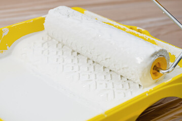 Painting apartment, renovating with white color paint. Paint roller in paint tray with white color in the tray on brown paper