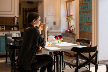 A young and beautiful girl sits in a cafe and has breakfast, drinks tea, and dreams. Inhales the aroma of tea, and basks in the sun.