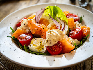 Salmon salad - smoked salmon hard boiled eggs, white cheese and green vegetables on wooden table

