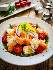 Salmon salad - smoked salmon hard boiled eggs, white cheese and green vegetables on wooden table
