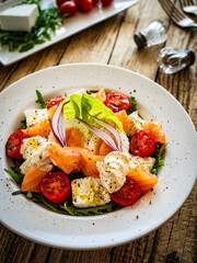 Salmon salad - smoked salmon hard boiled eggs, white cheese and green vegetables on wooden table
