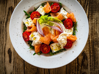 Salmon salad - smoked salmon hard boiled eggs, white cheese and green vegetables on wooden table
