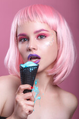 attractive young woman with pink bob cut and purple lips eating blue ice cream on pink background