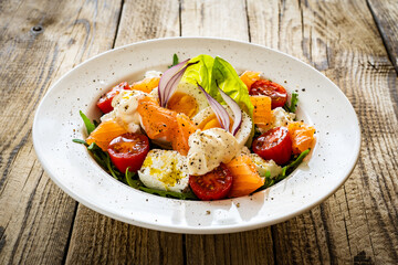Salmon salad - smoked salmon hard boiled eggs, white cheese and green vegetables on wooden table

