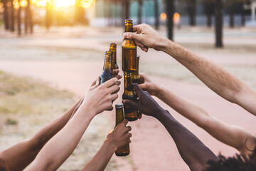 Group of multiracial young friends having fun celebrating together while cheering with beer bottles at summer party on vacation