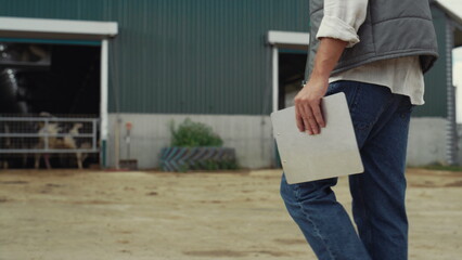 Farm worker walking livestock facility. Hand holding clipboard legs closeup.