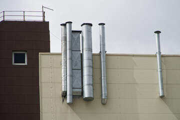 A variety of steel exhaust ventilation pipes on the outer wall of an industrial or office building.