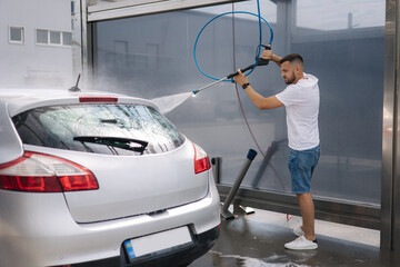 Back view of young man cleaning his car with a jet sprayer. Self service car washing