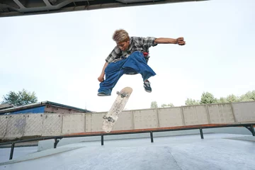 Fotobehang Skateboard Portrait of teenage boy doing skateboard tricks in air at outdoor skatepark in urban area  © Seventyfour