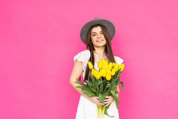 Spring flowers. Young woman in a bright pink dress is looking in the camera with a big smile, holding a bunch of tulips in her hands.