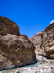 Fototapeta na wymiar A river flowing between rocks along an asphalt road on blue sky background