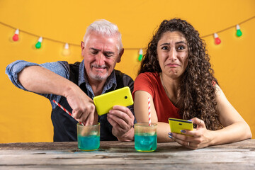 father and daughter have fun putting a smartphone into a glass full of a blue cocktail