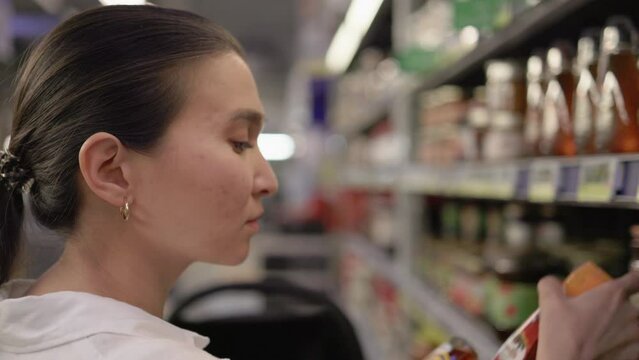 Brunette woman in white choosing products on supermarket's shelves