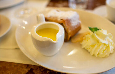 Austrian sweet dessert, portion of apple strudel with whippen cream and hot vanilla sauce served in old bakery cafe in Vienna, Austria