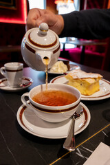Tea time in England, pouring of black earl grey tea with bergamot in cafe in London, high tea