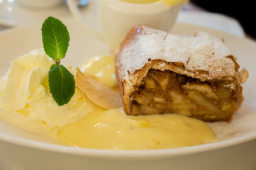Austrian sweet dessert, portion of apple strudel with whippen cream and hot vanilla sauce served in old bakery cafe in Vienna, Austria