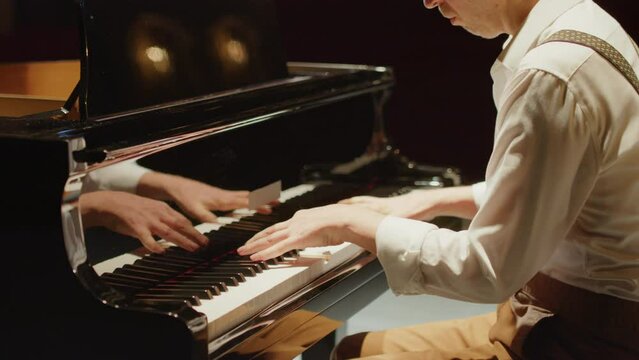Cropped arc shot of male pianist playing grand piano on stage in concert hall