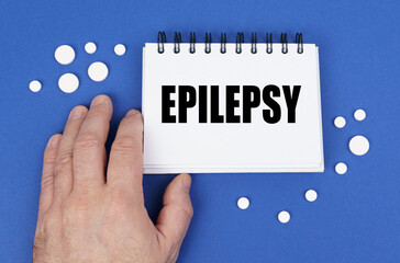 On the blue surface of the tablet, a hand and a notepad with the inscription - EPILEPSY