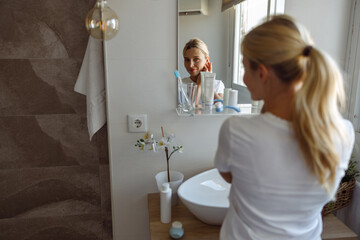 Skincare concept. Young beautiful lady looking at herself in mirror and smiling.