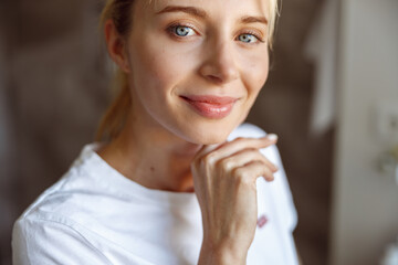 Face of young attractive Caucasian woman touching chin with hand and smiling. Portrait.