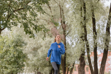 Naklejka na ściany i meble a European woman in a blue hoodie is running and doing sports in the park. selective focus, fitness and yoga outdoor sports, exercise and meditation and fitness for body health. spiritual development