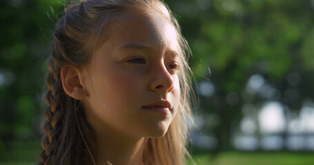Thoughtful pretty girl looking in distance in city park closeup. Golden sunlight