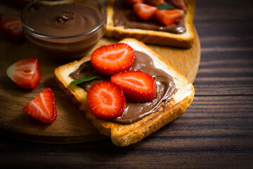 Toasted bread with chocolate spread strawberries on a wooden background