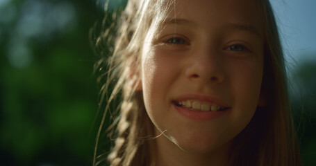 Fototapeta premium Cheerful blond girl posing in golden sunlight. Playful child looking in camera 