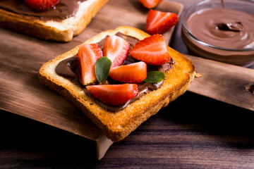 Toasted bread with chocolate spread strawberries on a wooden background