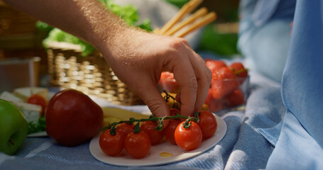 Unknown human hands take tomatoes on picnic closeup. Man arm hold red vegetables