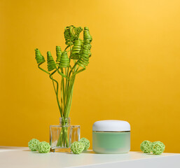 Green jar for cosmetics on a white table. Packaging for cream, gel, serum, advertising and product promotion
