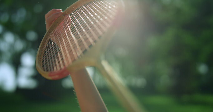 Closeup hand holding wooden badminton racket in golden sunlight in park.