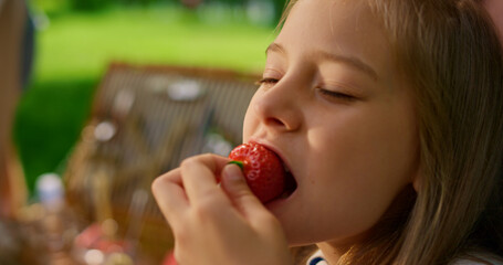 Pretty girl eating strawberry on summer picnic close up. Blond child taste berry